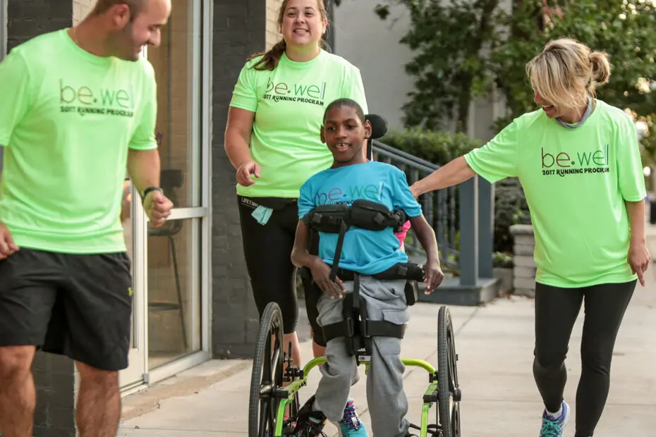 A boy in a wheelchair is joined on a walk by a group of smiling adults
