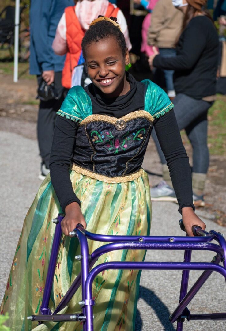 A girl with a walker and dressed as a princess smiles at the be.well Halloween Hike