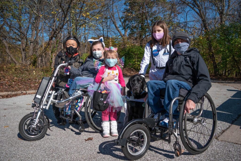 A family with people using wheelchairs poses at the be.well Halloween Hike