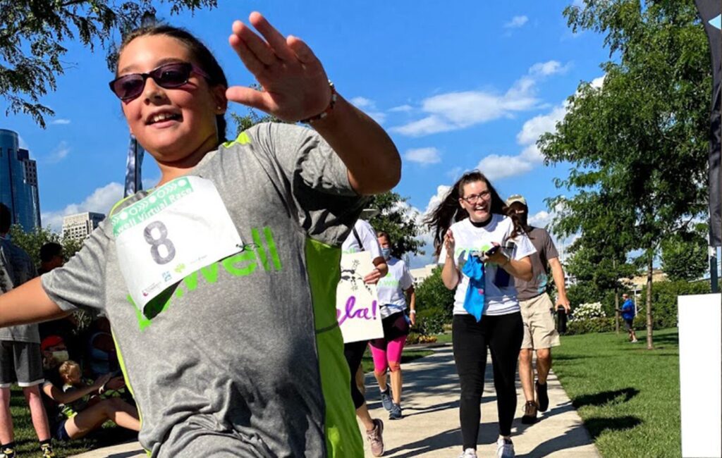 A race crosses the finish line while her family cheers in the background