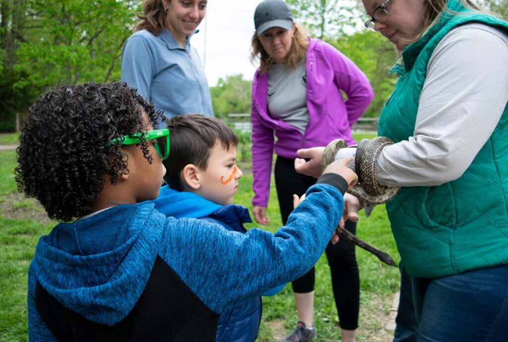 A child touch a snake that a Cincinnati Parks Explore Nature naturalist is holding