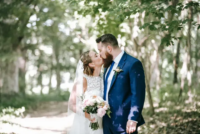 A bride and groom on their wedding day, kissing while staning in the woods.