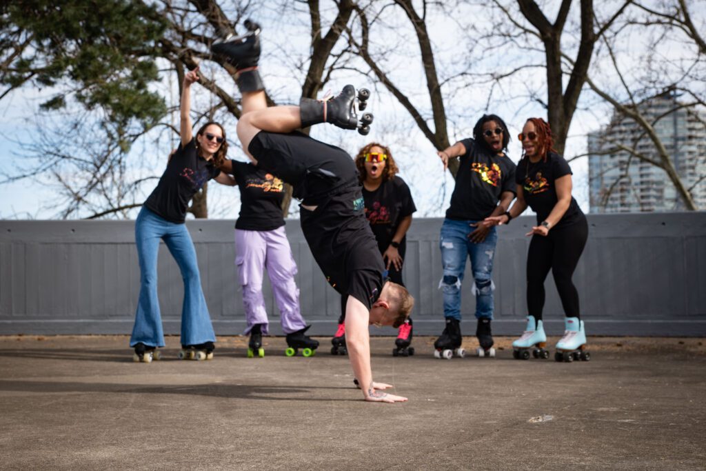 A group of roller skaters watches a man on roller skates do a hand stand