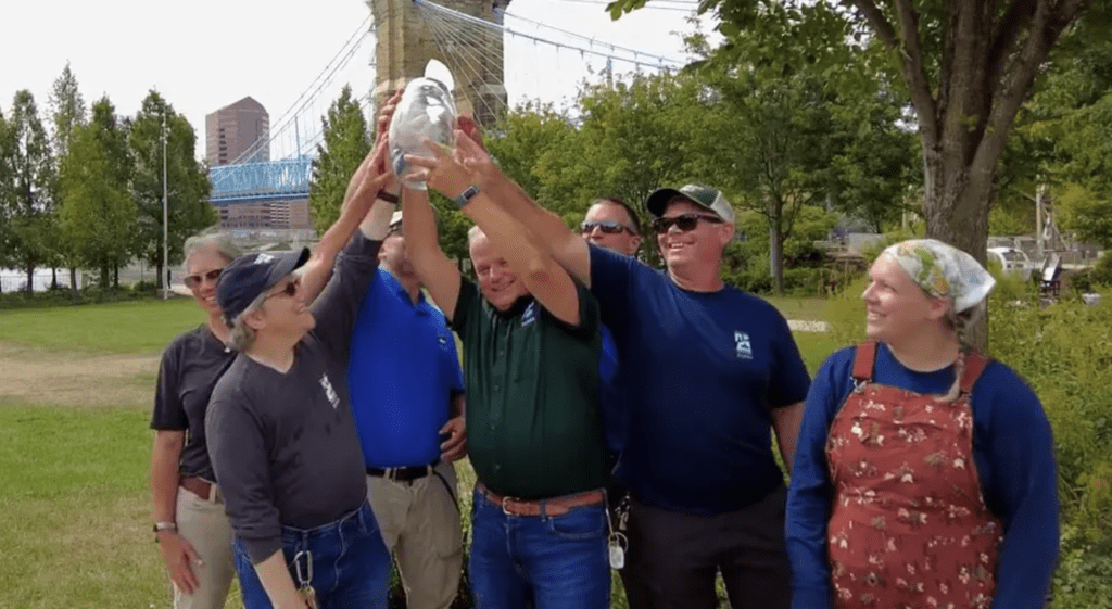 A group of people holding up an award in front of a bridge.